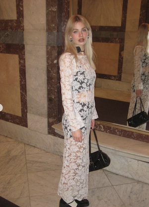 blonde woman wearing white lace maxi dress and a black rose choker necklace looking at the camera