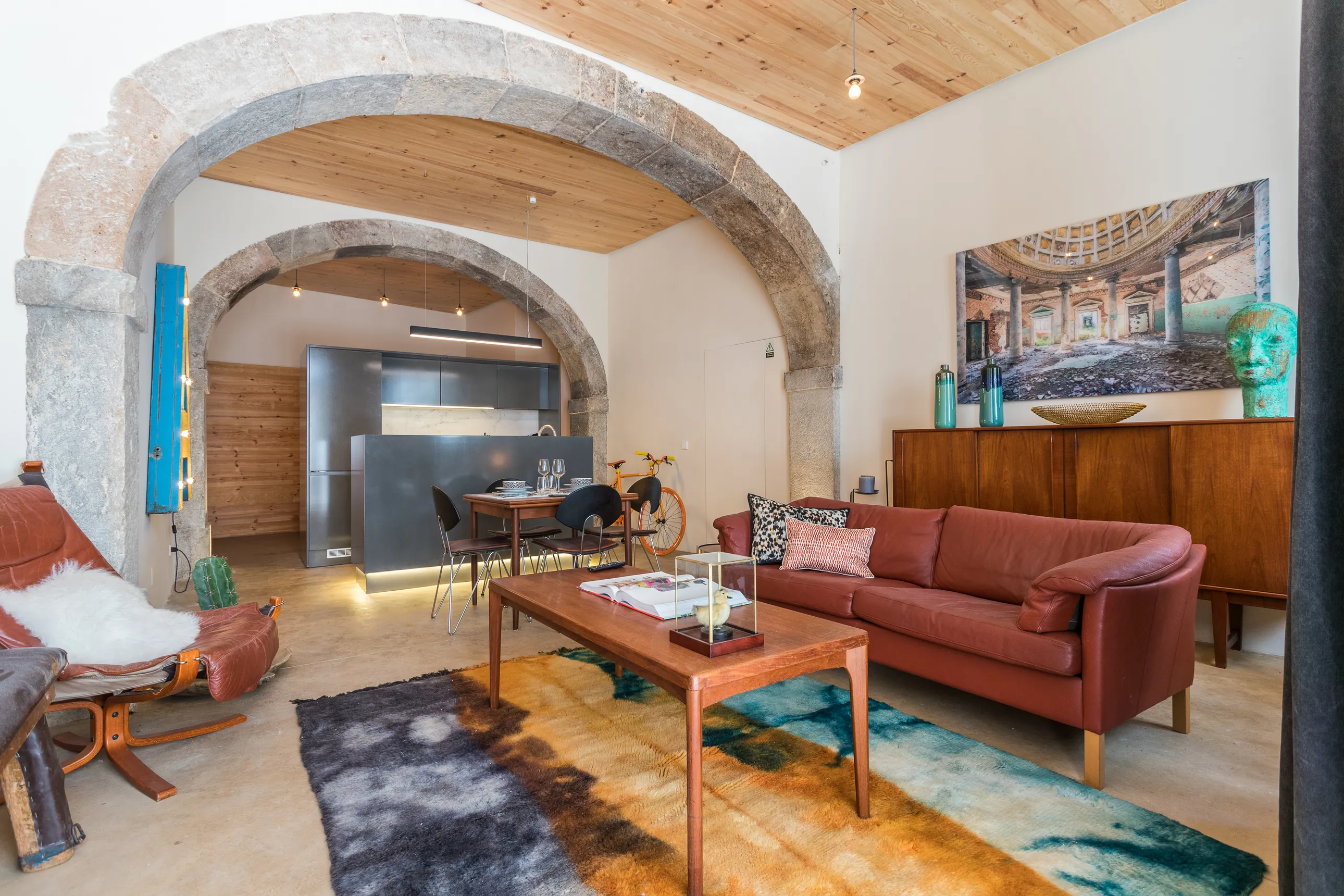 a living room with two stone archways, a brown couch, colored rug