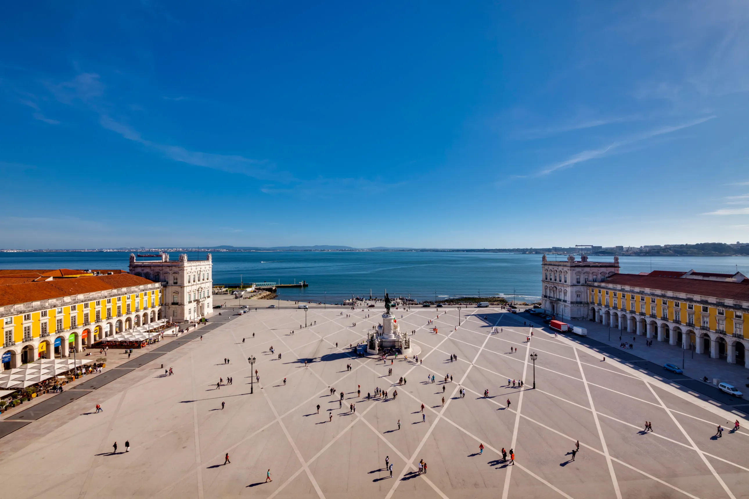 a square with a statue in the middle next to the water and buildings