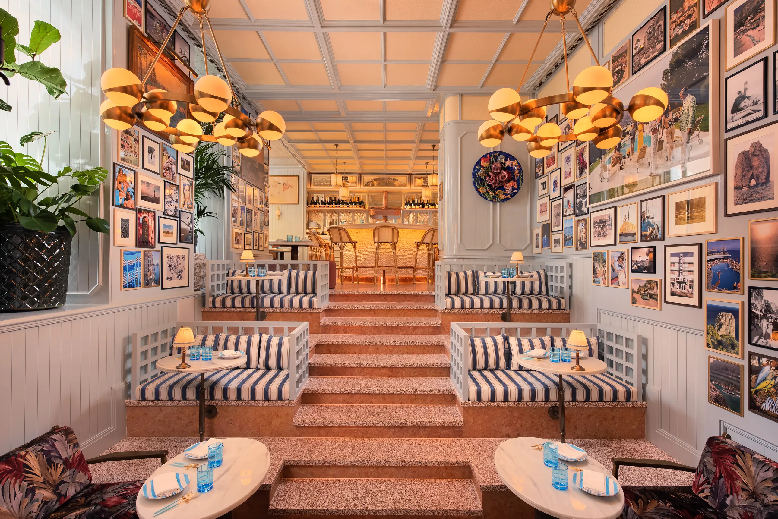 a lobby with a stairway in the center and striped chairs on each side, paintings and lighting on the walls