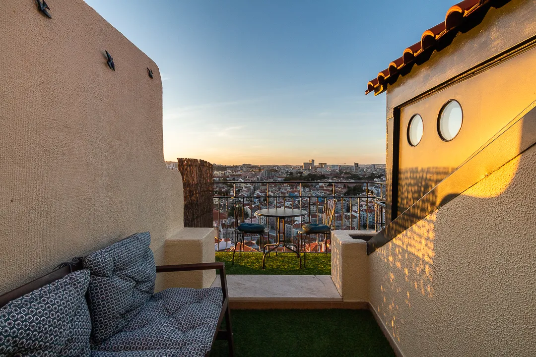 outside view on the balcony in between two walls with a bench, table, chairs overlooking the city