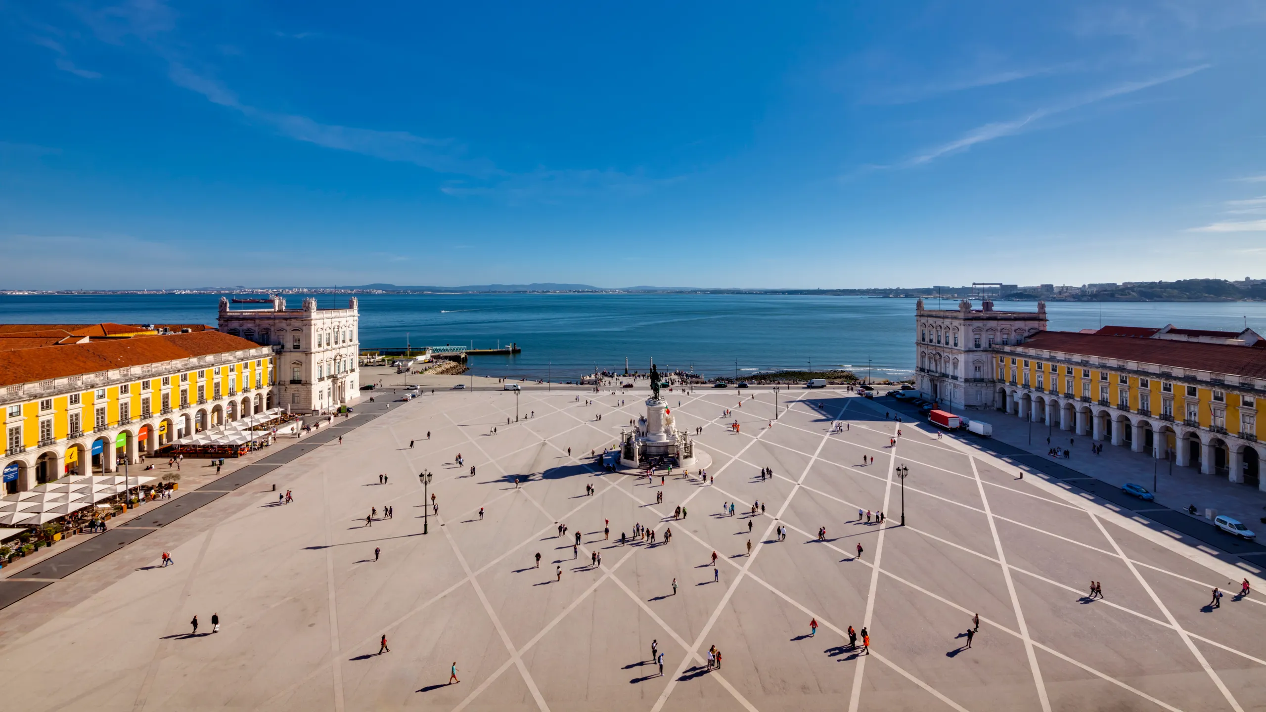 a square with a statue in the middle next to the water and buildings