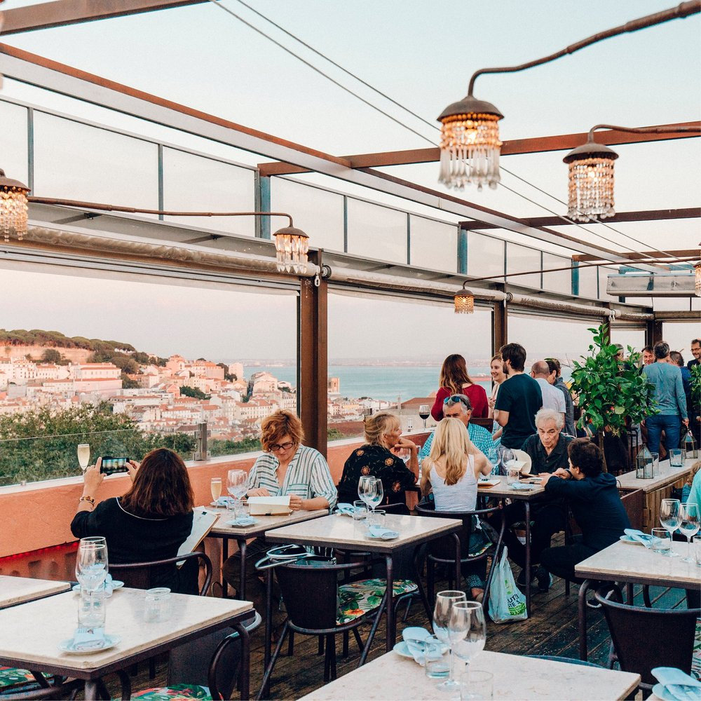 different people sitting at tables on a rooftop overlooking Lisbon