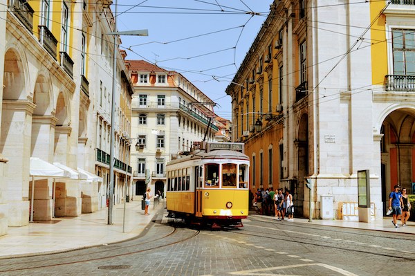 yellow tram riding down the street between white and yellow buildings