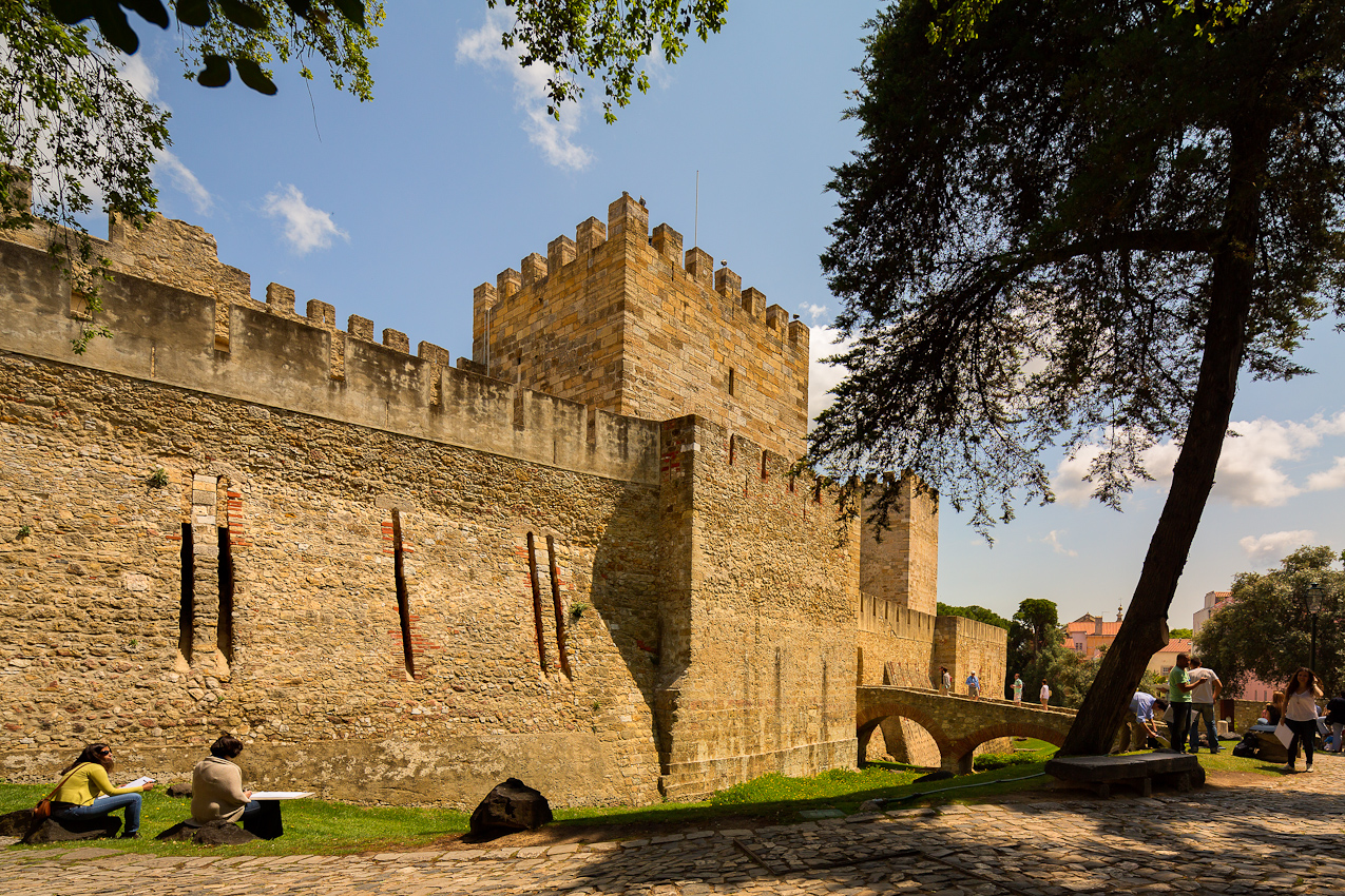 a castle with a bridge and tourists surrounding it