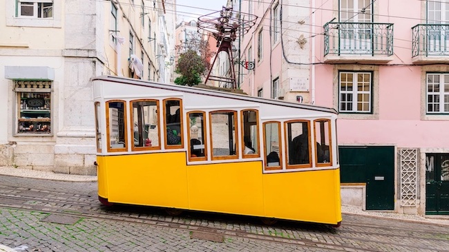 yellow tram riding down the street between white and yellow buildings