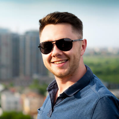 headshot of a brunette man wearing dark sunglasses smiling outside